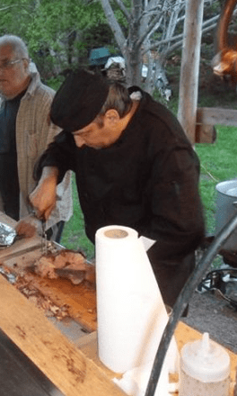 Chef de Méchoui du Marquis découpant des viandes grillées au feu de bois pour un service traiteur en plein air au Québec, lors d’un évènement festif