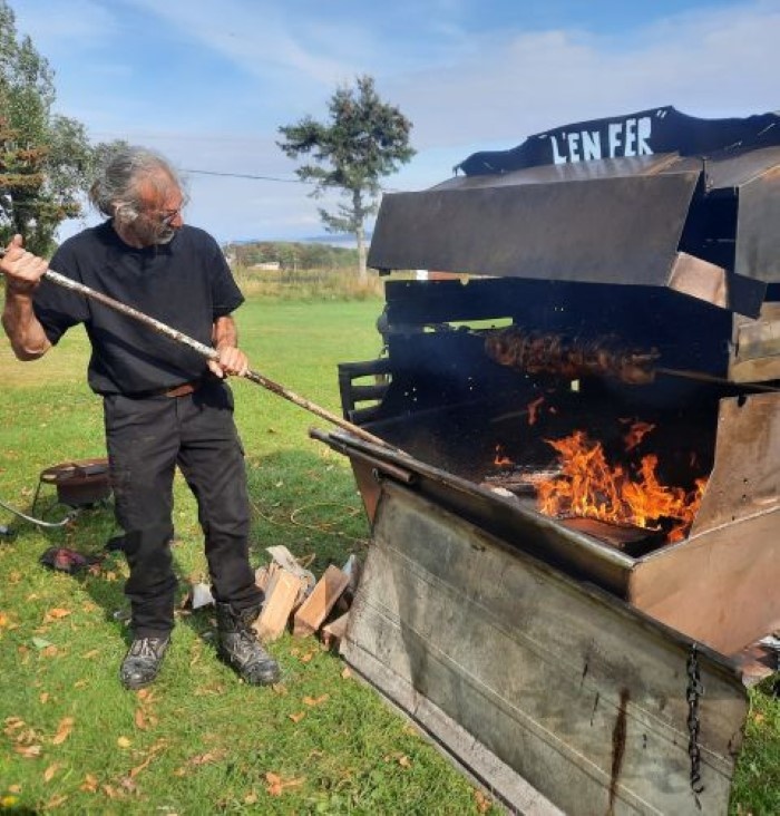 Chef de Méchoui du Marquis ajustant la cuisson au feu de bois pour un méchoui traditionnel en plein air au Québec, avec rôtissoire et viandes grillées pour évènements et réceptions